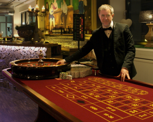 Ein Croupier am Roulettetisch, der gerade in edelem Ambiente den Roulettekessel dreht