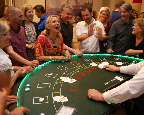 Ein voller Black Jack Tisch. Eine Spielerin hat gewonnen und lacht triumphierend den Croupier an. Die anderen Gäste freuen sich für sie.