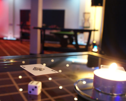 Ein Würfel und eine Spielkarte, im Hintergrund weitere Casinotische und eine Pop-up-Wand mit Las Vegas-Motiv